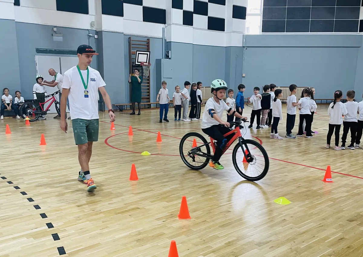 Copil pe bicicletă în poligonul EcoRider din sala de sport, cu trainerul alături