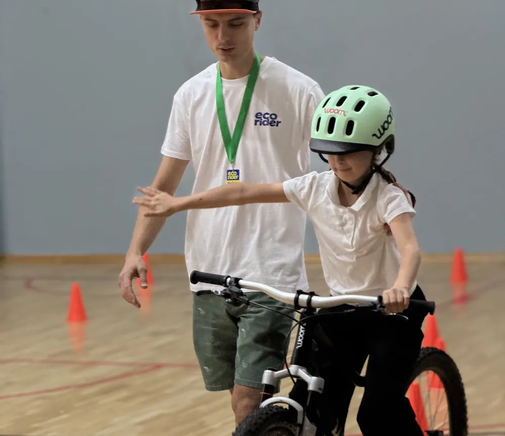 Fetiță pe bicicletă, ghidată de un trainer EcoRider care îi corectează poziția